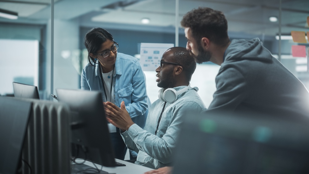 Diverse Group of Professionals Meeting in Modern Office: Energetic and Enthusiastic IT Programmers Use Computer Together, Talk cybersecurity Strategy, Discuss Planning. Software Engineers Develop Inspirational App