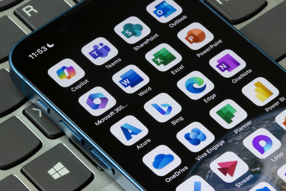 Assorted Microsoft apps are seen on an iPhone, including Copilot, Teams, SharePoint, Outlook, 365, Word, Excel, PowerPoint, Azure, Bing, Edge, OneNote, OneDrive, etc
